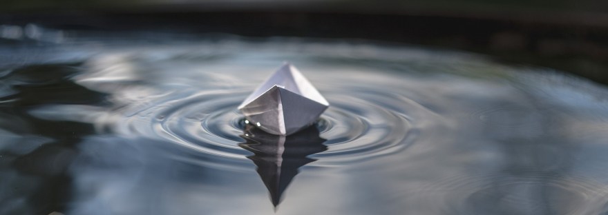 A paper boat floating calmly on water, symbolizing release, surrender, and the energy of allowing.
